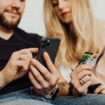 A couple using a smartphone and credit card for online shopping indoors.