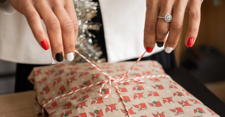 Close-up of a woman unwrapping a Christmas gift with festive decorations and tinsel.