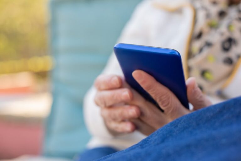 Senior adult using a smartphone outdoors on a sunny day. Focus on hands and device.